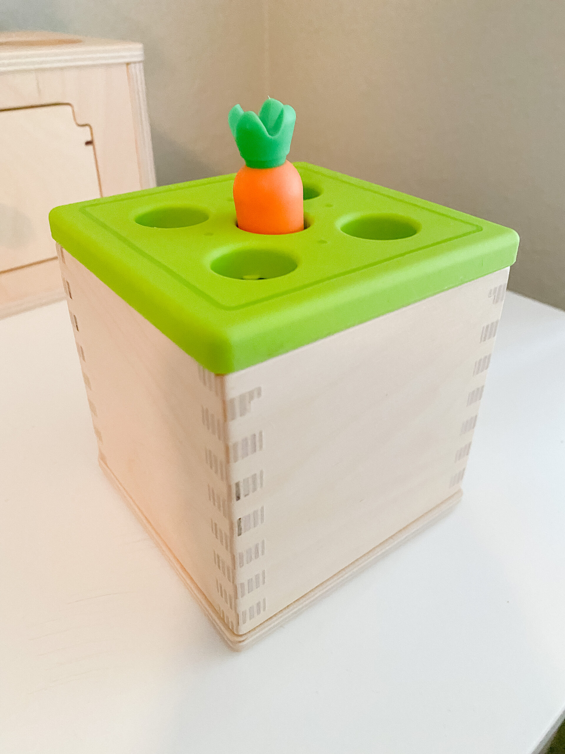 Photo shows a wooden baby toy with a green top and a play carrot sticking out of the top.