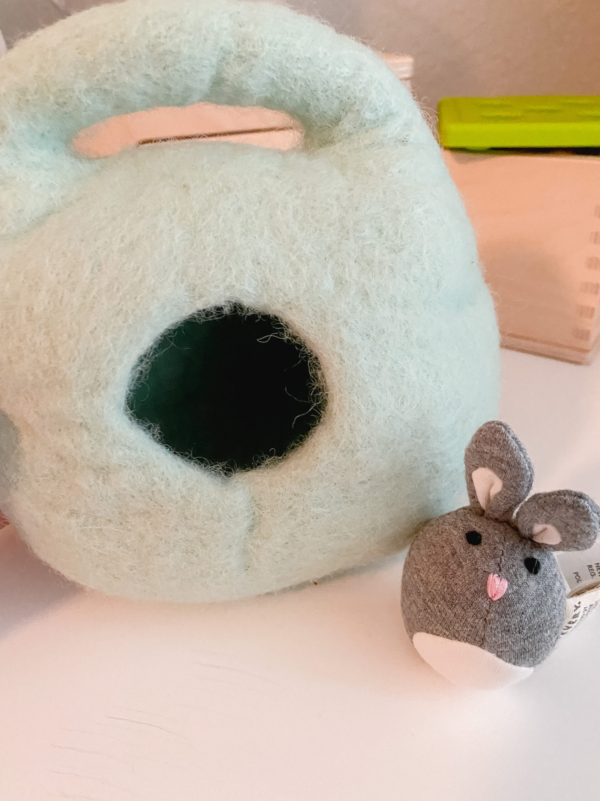 Photo features a green felted wool burrow with a small grey bunny toy in front of it.
